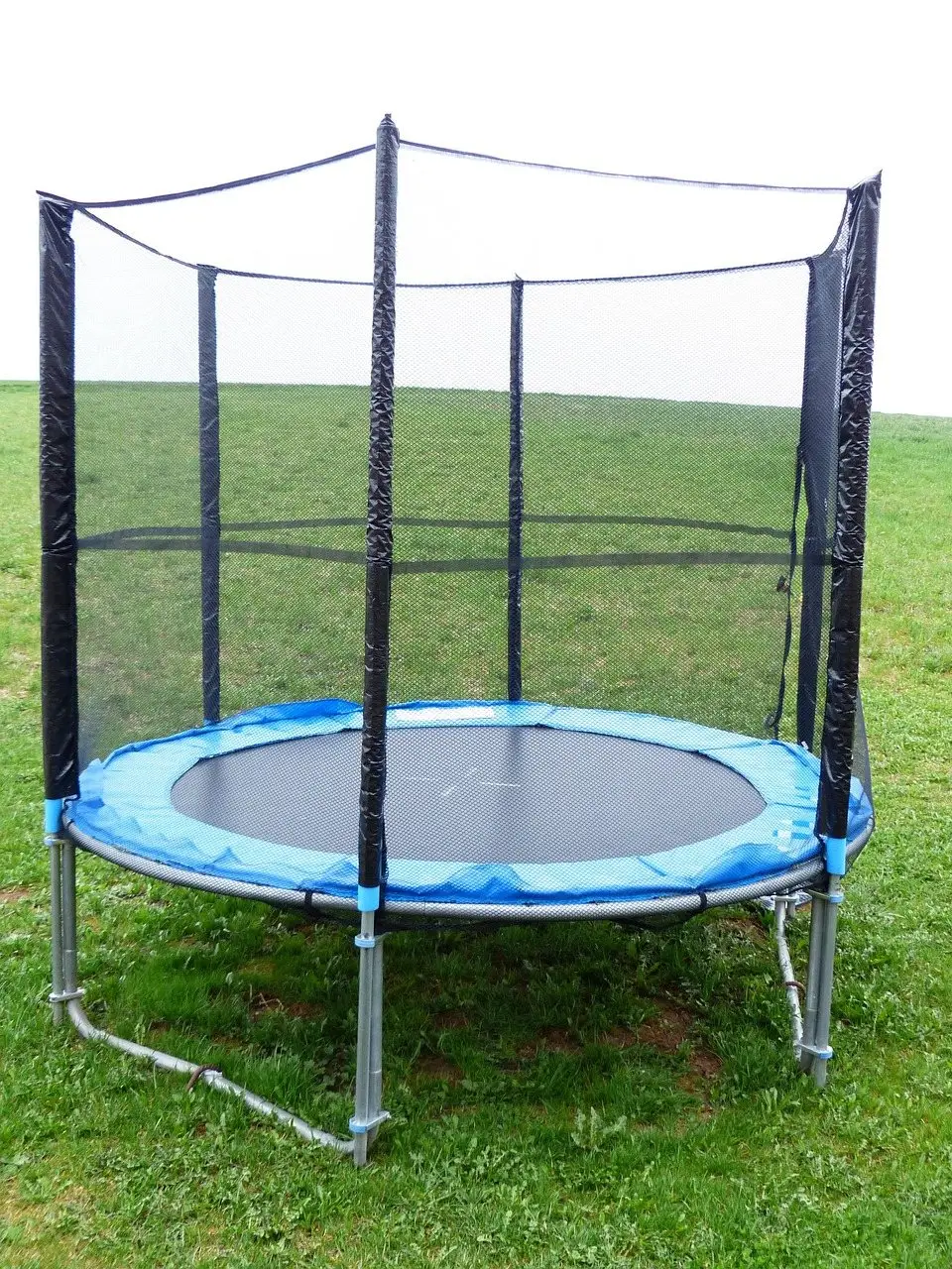 A round garden trampoline with a blue frame pad and a safety enclosure on a lawn