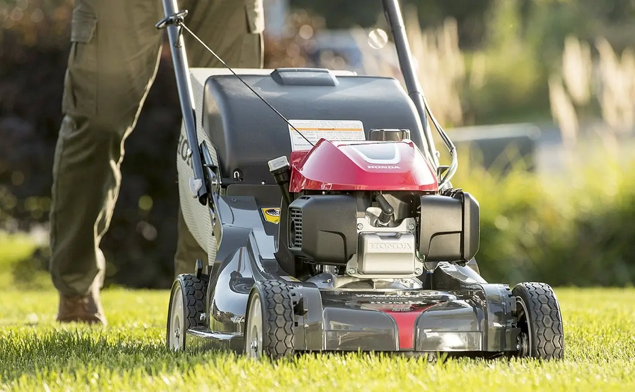 A walk-behind petrol mower on a lawn, deck and front wheels in close view