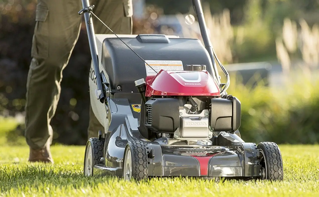 A walk-behind petrol mower on a lawn, deck and front wheels in close view