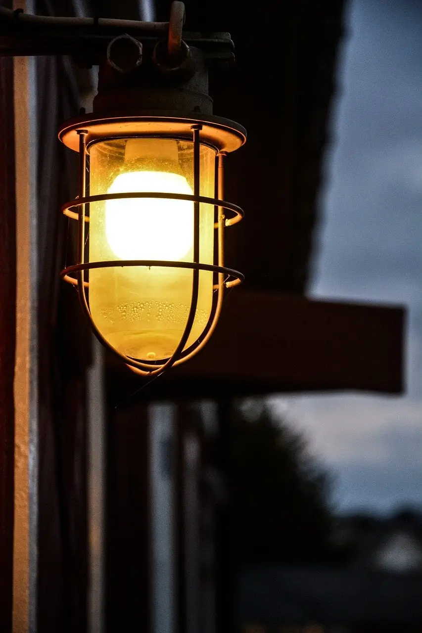 A caged wall lantern glowing warm yellow against a dark building at night