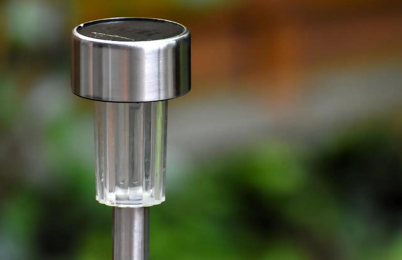 A stainless steel solar path light, its small photovoltaic panel visible on top