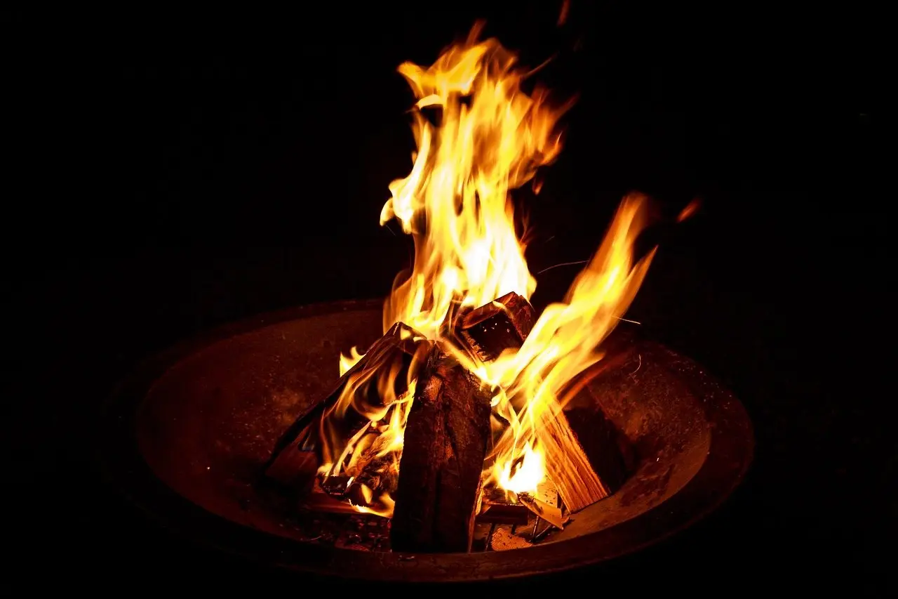 Split logs burning with tall flames inside a round steel fire bowl at night