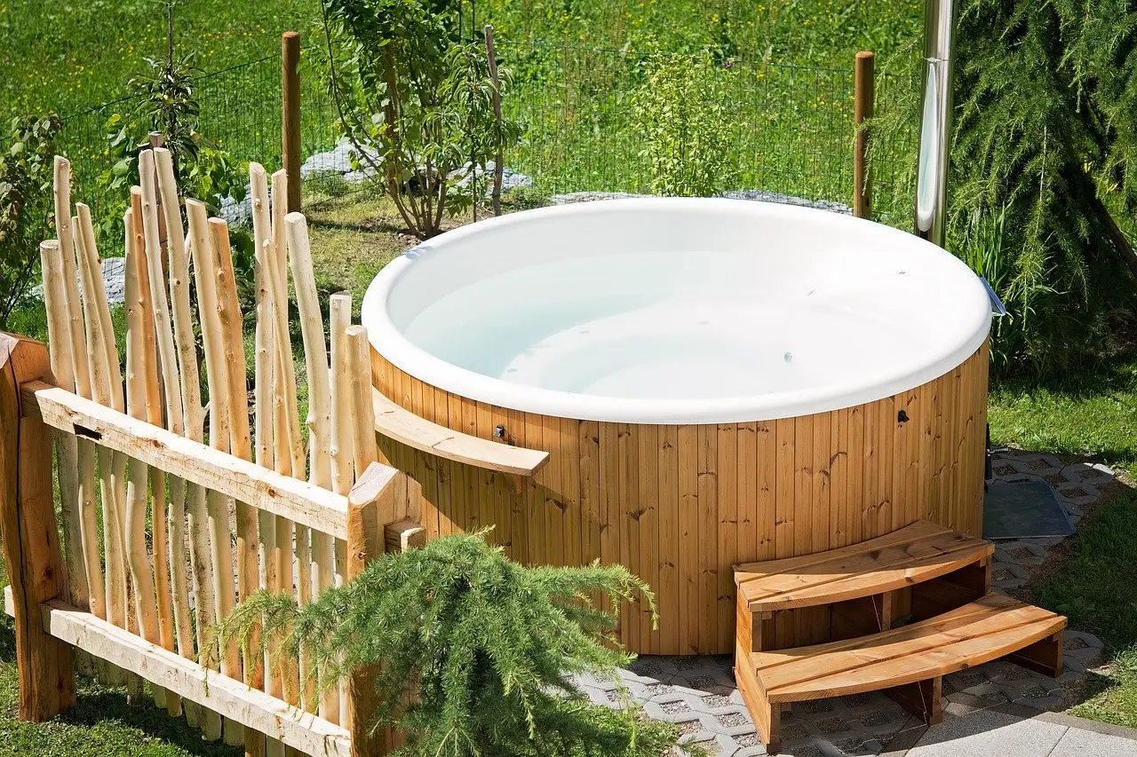 A small round timber-clad hot tub on a paved base in a garden, with wooden steps alongside