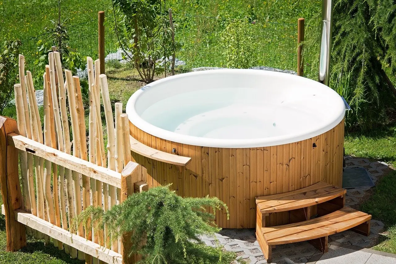 A small round timber-clad hot tub on a paved base in a garden, with wooden steps alongside