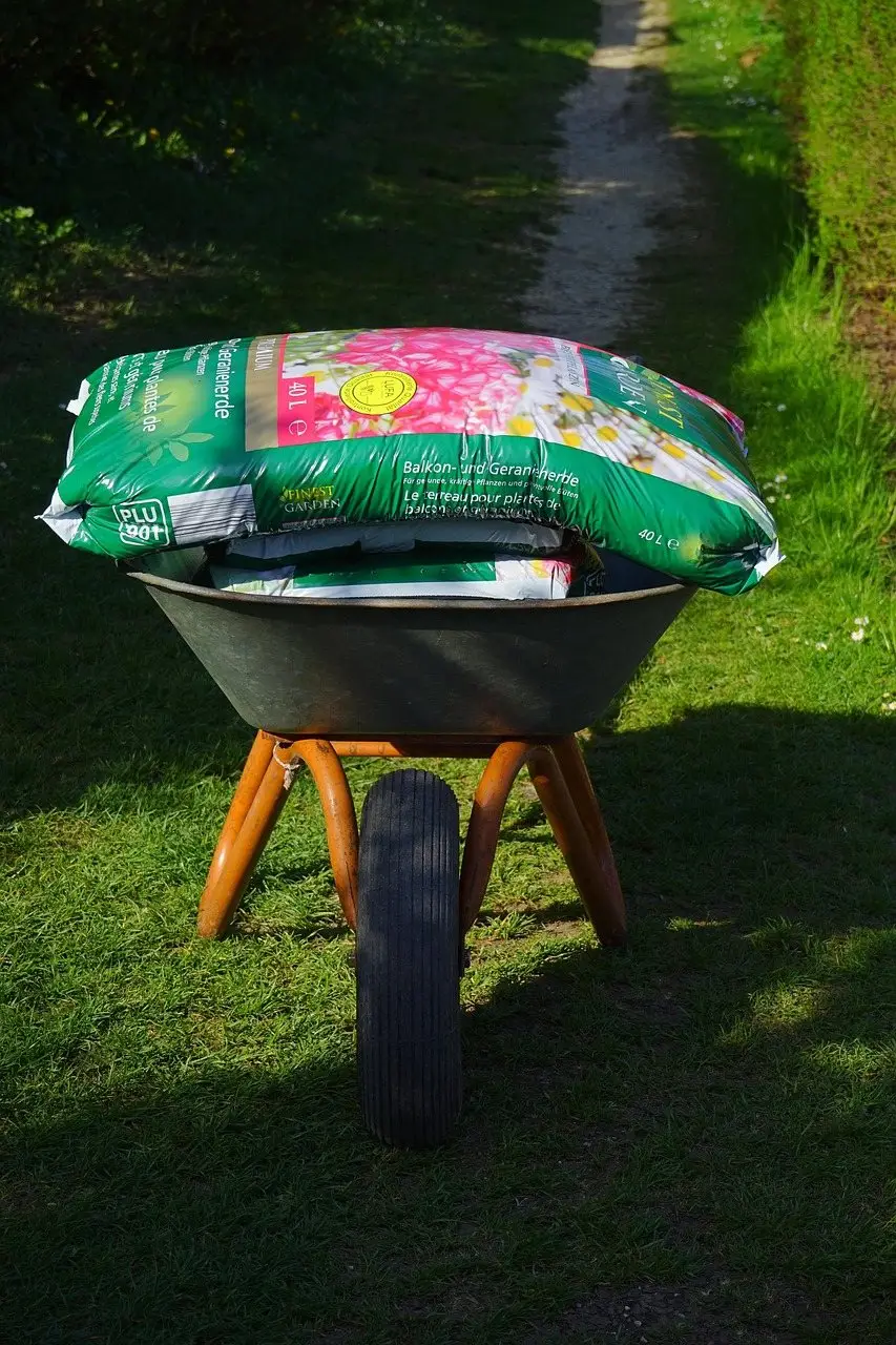 A bag of compost resting in a wheelbarrow on a lawn