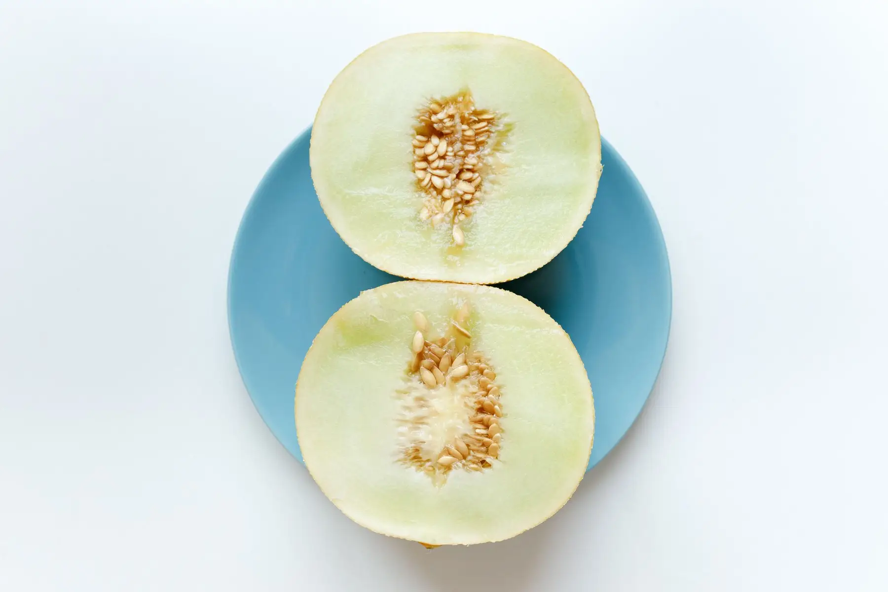 A honeydew melon cut in half on a plate, pale green flesh with the seed cavity exposed