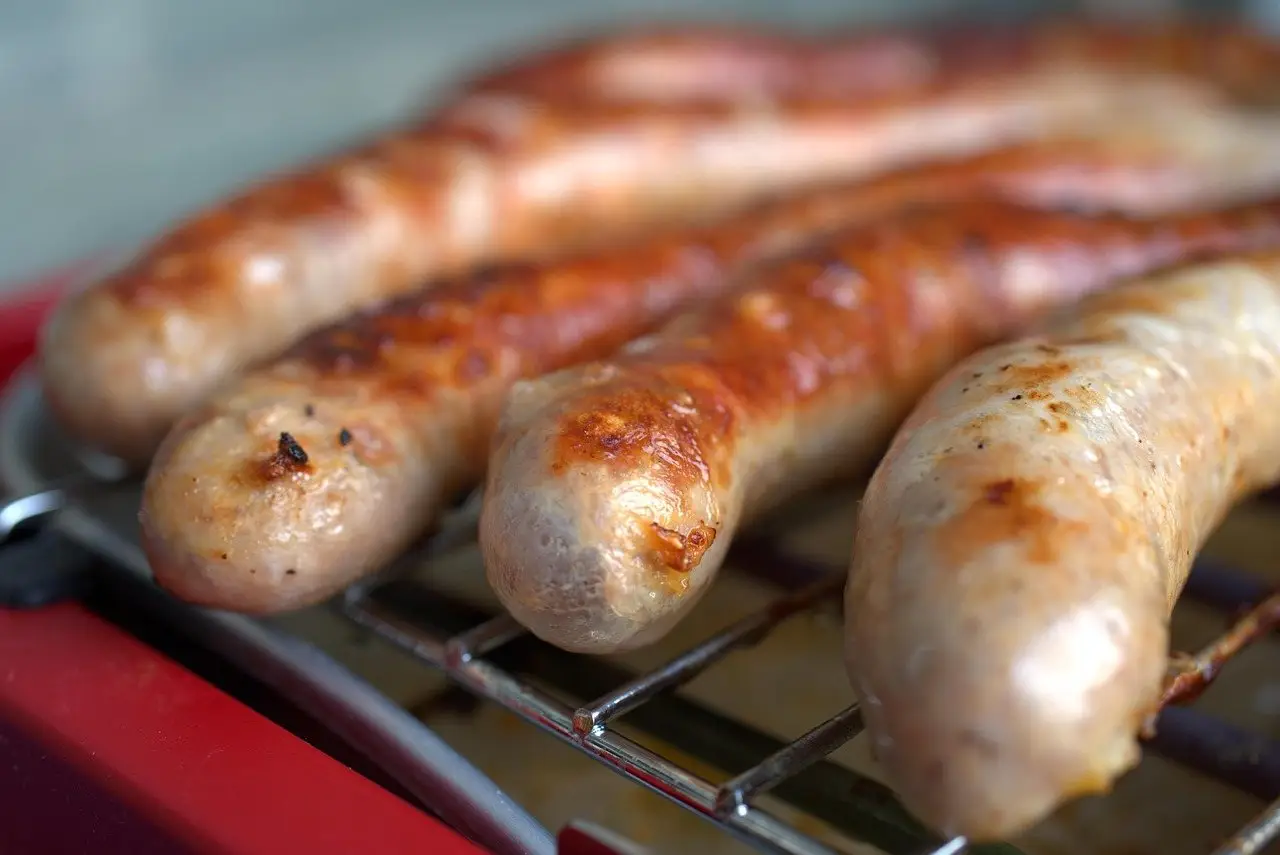 Sausages cooking on the bars of a small charcoal grill