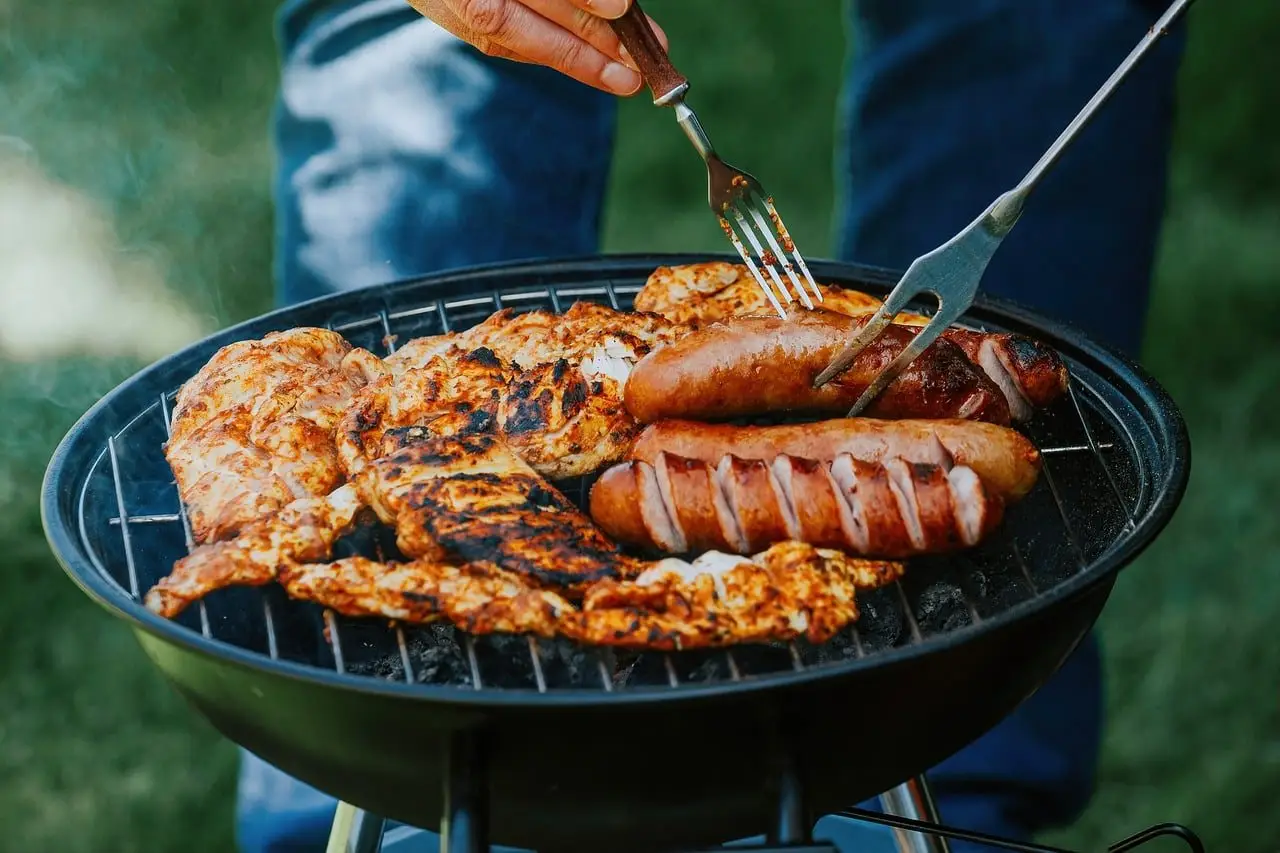 Chicken and sausages cooking on the bars of a round charcoal grill