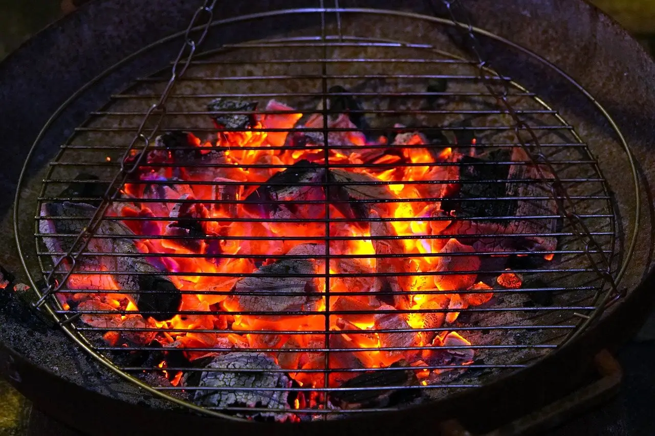 A round grill grate seen from above over a bed of glowing orange coals