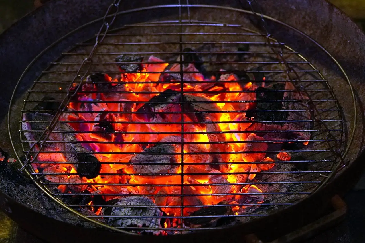 A round grill grate seen from above over a bed of glowing orange coals