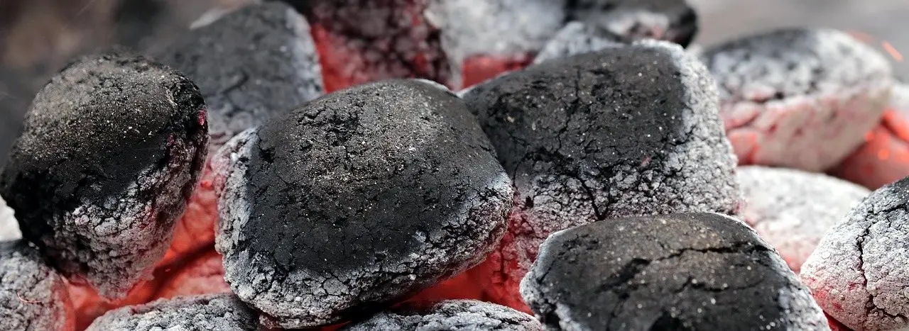 Charcoal briquettes burning down to grey ash with red embers glowing between them
