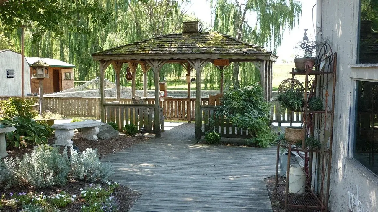A timber garden pavilion with a solid shingled roof beside a planted border