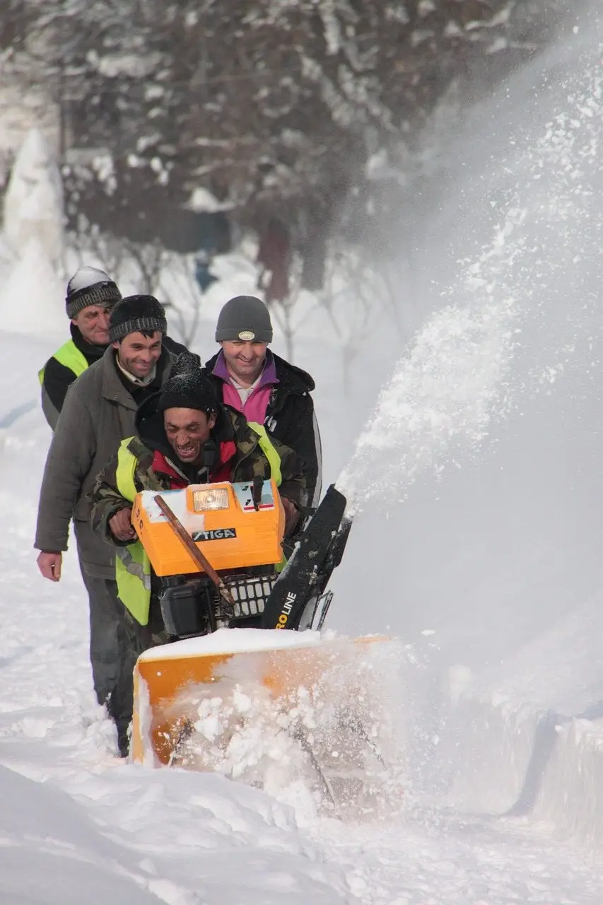 People clearing deep snow with a petrol snow blower throwing a plume