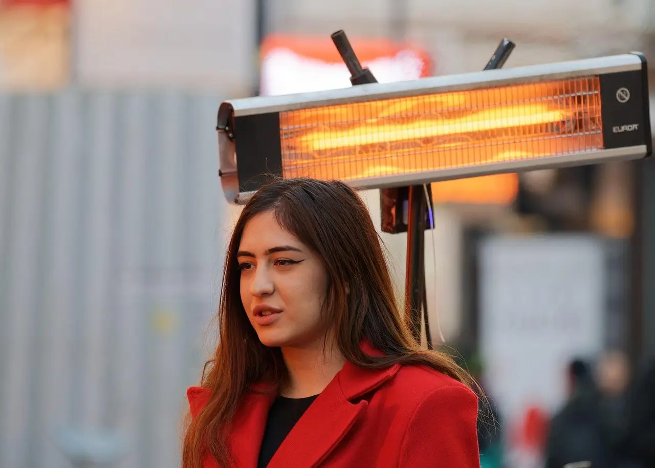 An electric radiant heater glowing on a bracket above a person seated on an outdoor terrace