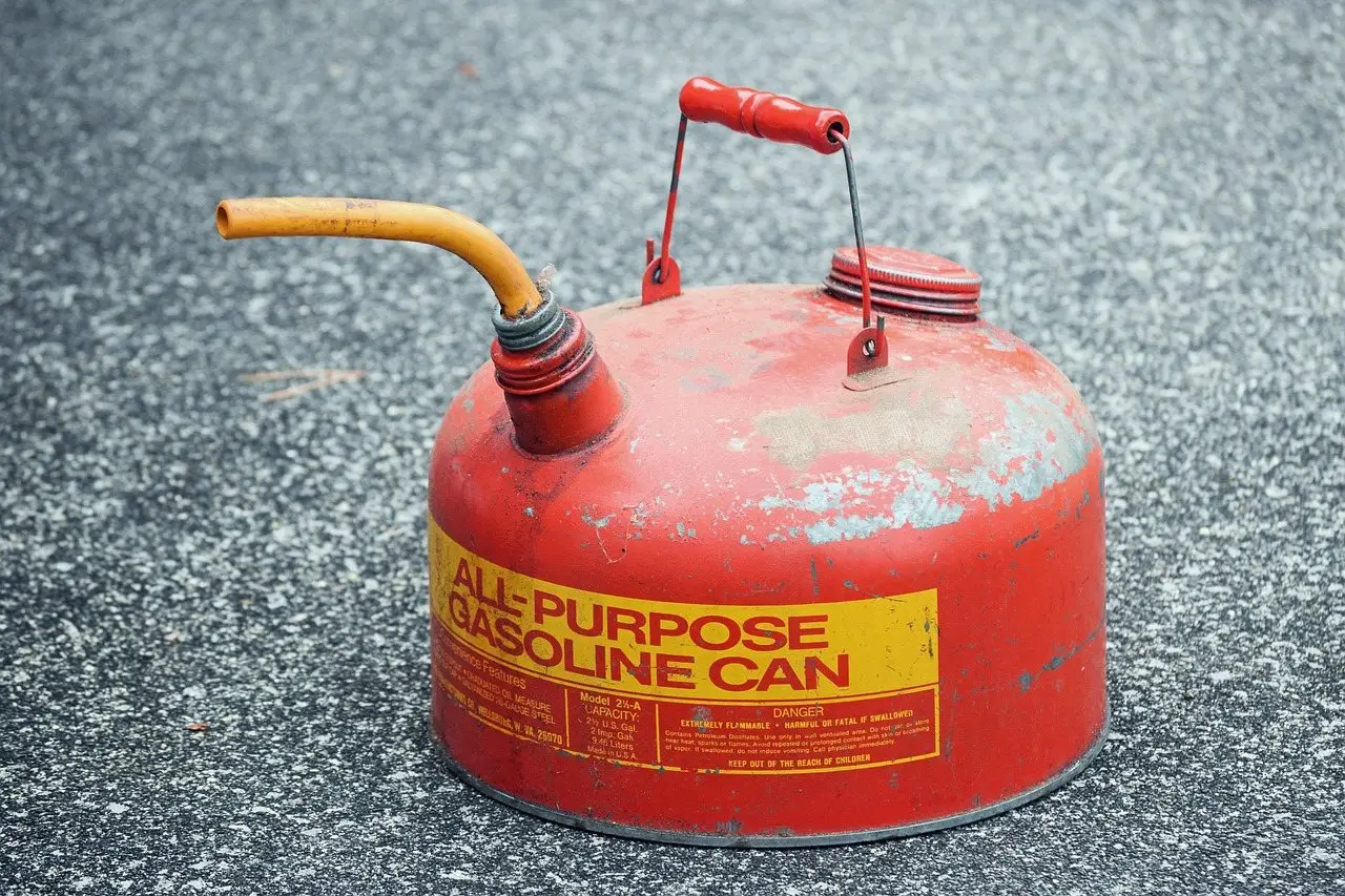 A weathered red metal gasoline can with a flexible spout standing on tarmac