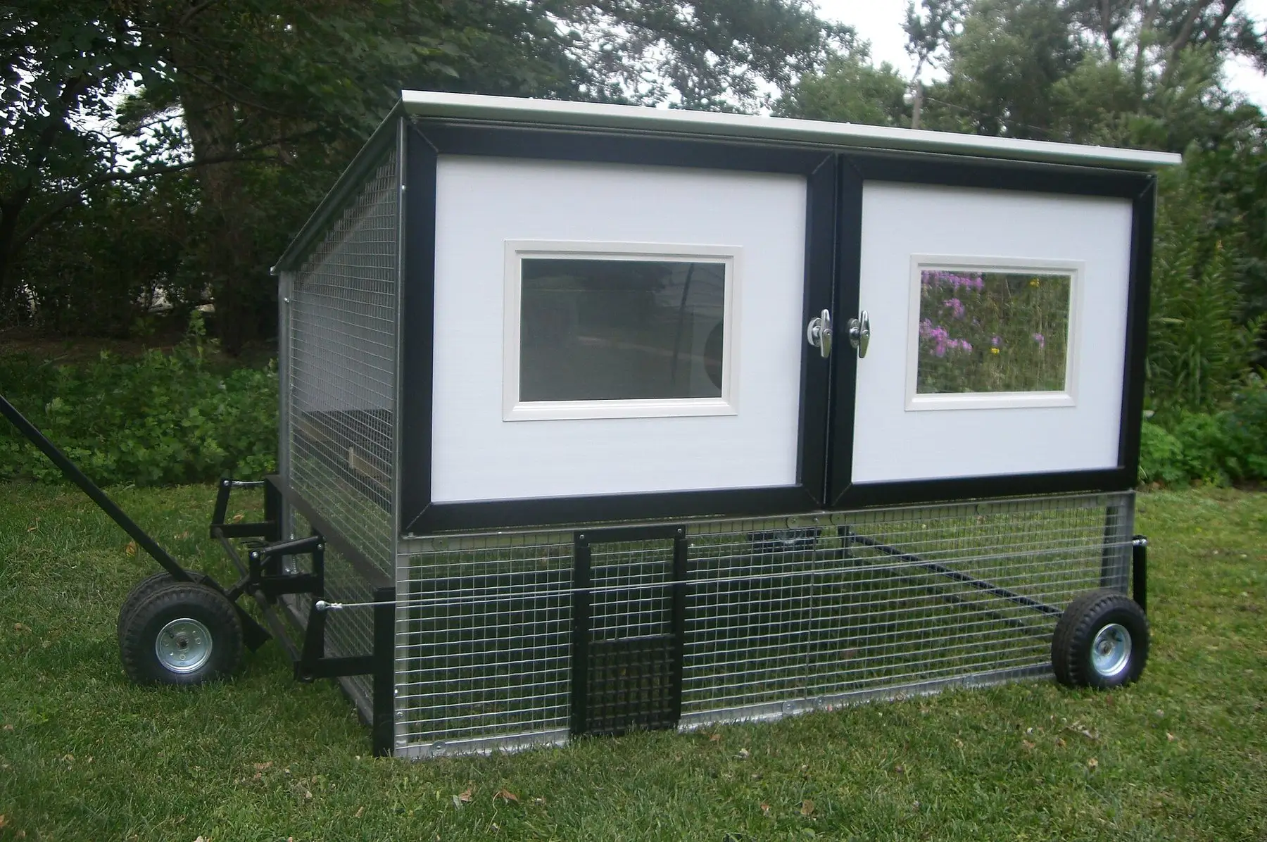 A mobile chicken coop on wheels with an enclosed wire run beneath it