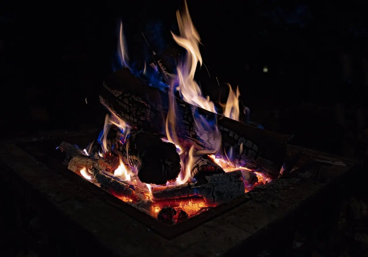 Logs burning in a square built fire pit at night, flames and glowing embers at the base