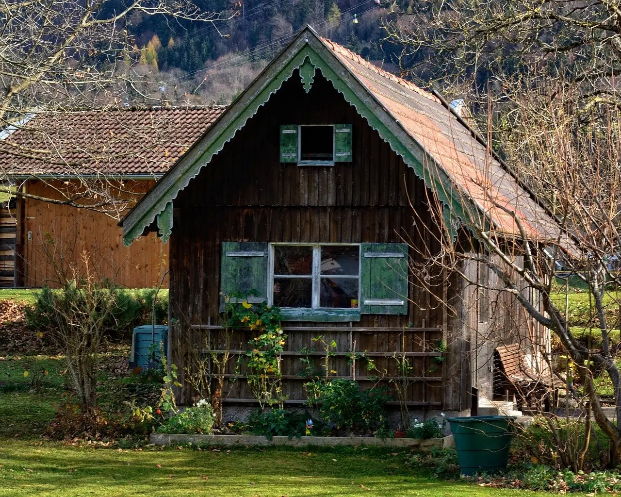 A timber garden cabin with decorative bargeboards and shuttered windows standing on a lawn