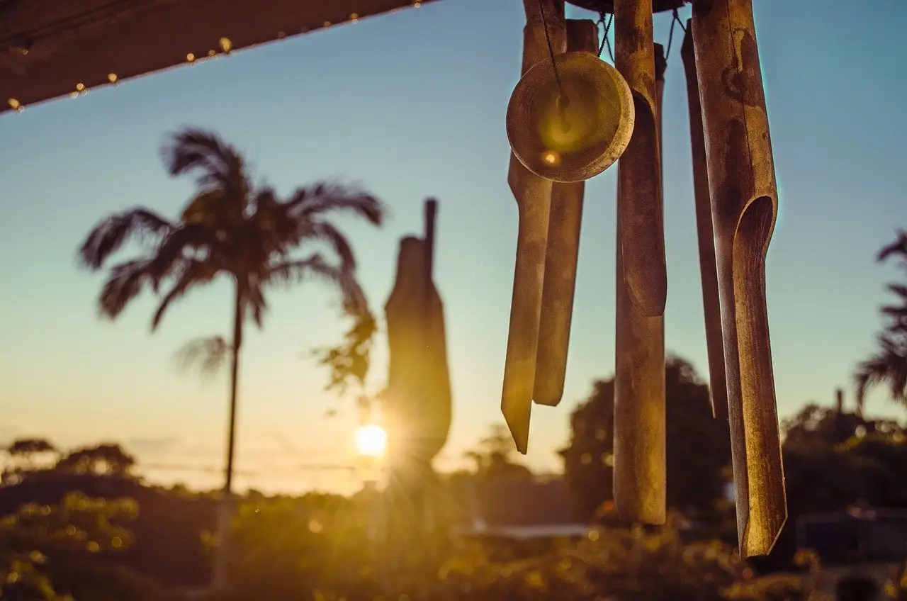 Wooden and metal wind chimes hanging from a patio beam in low evening sun