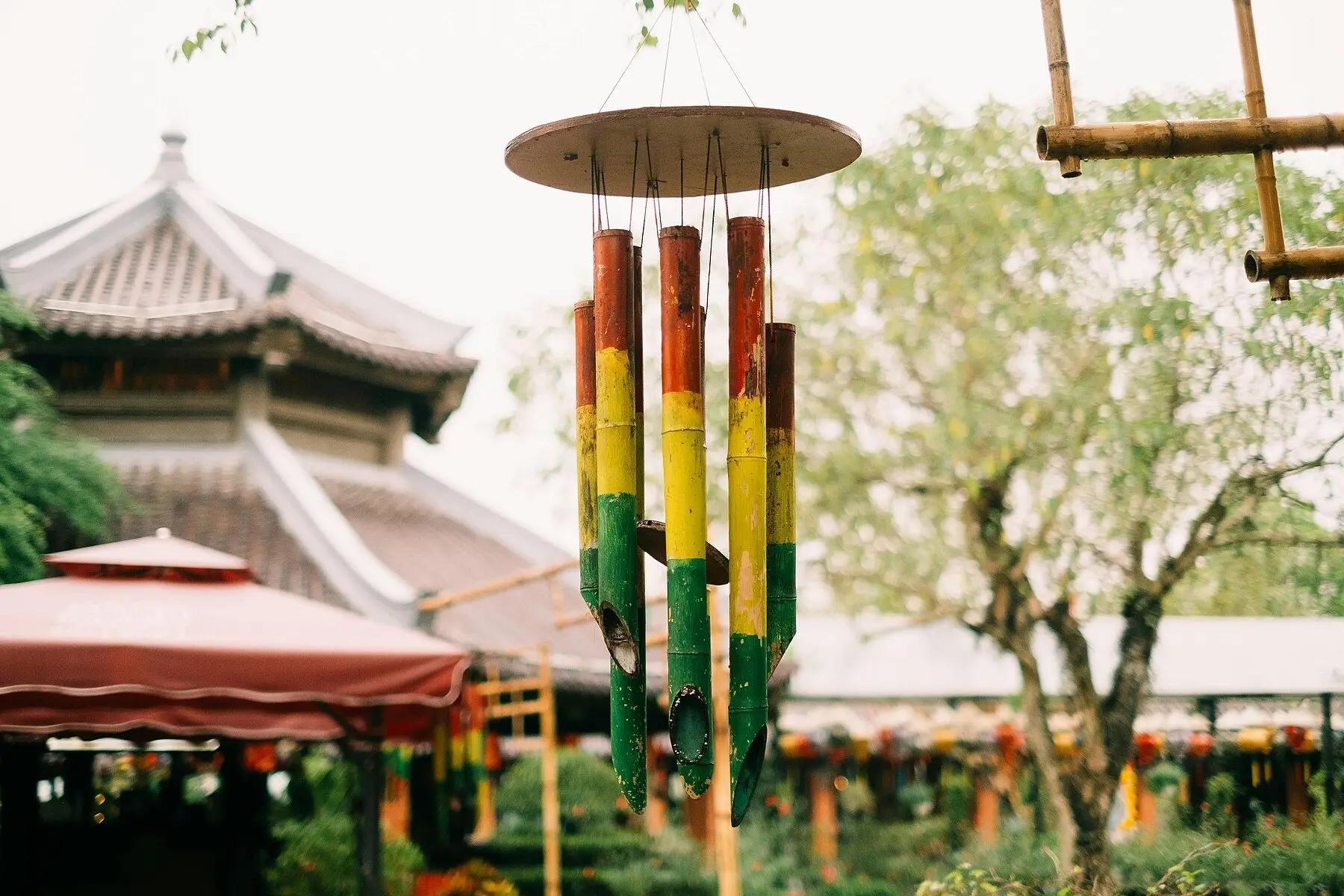 A painted bamboo wind chime hanging in a garden, its tubes catching the light
