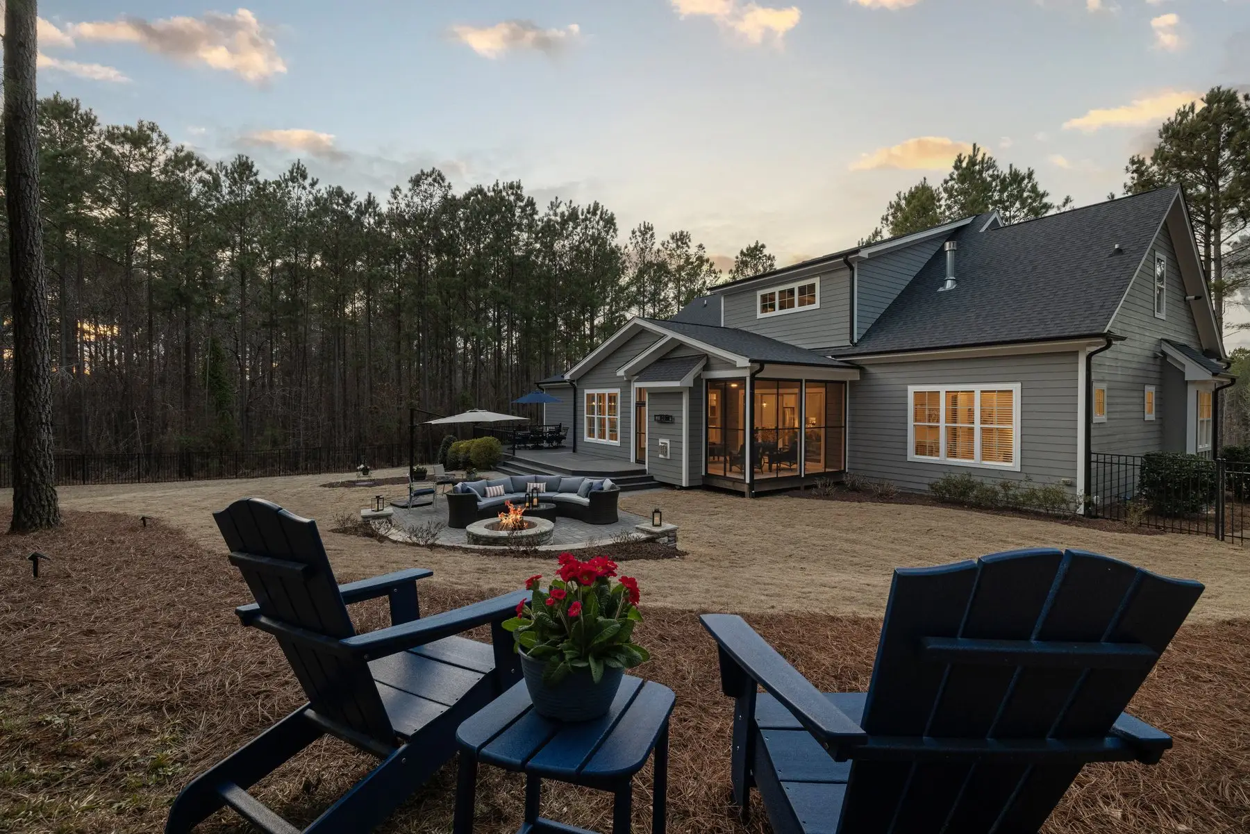 A lit fire pit on a paved patio set well back from a house, with open sky above and nothing overhanging it