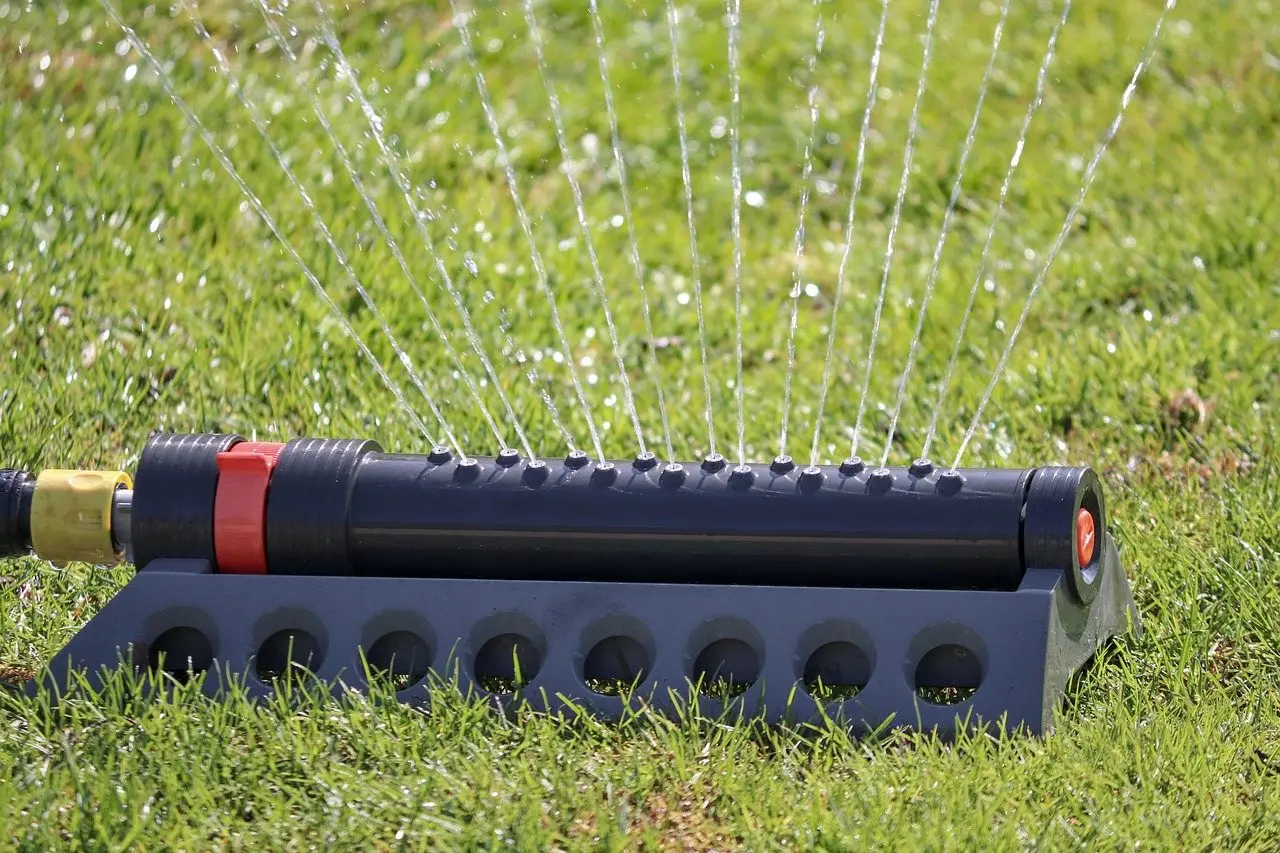 An oscillating sprinkler throwing fine jets of water across a green lawn