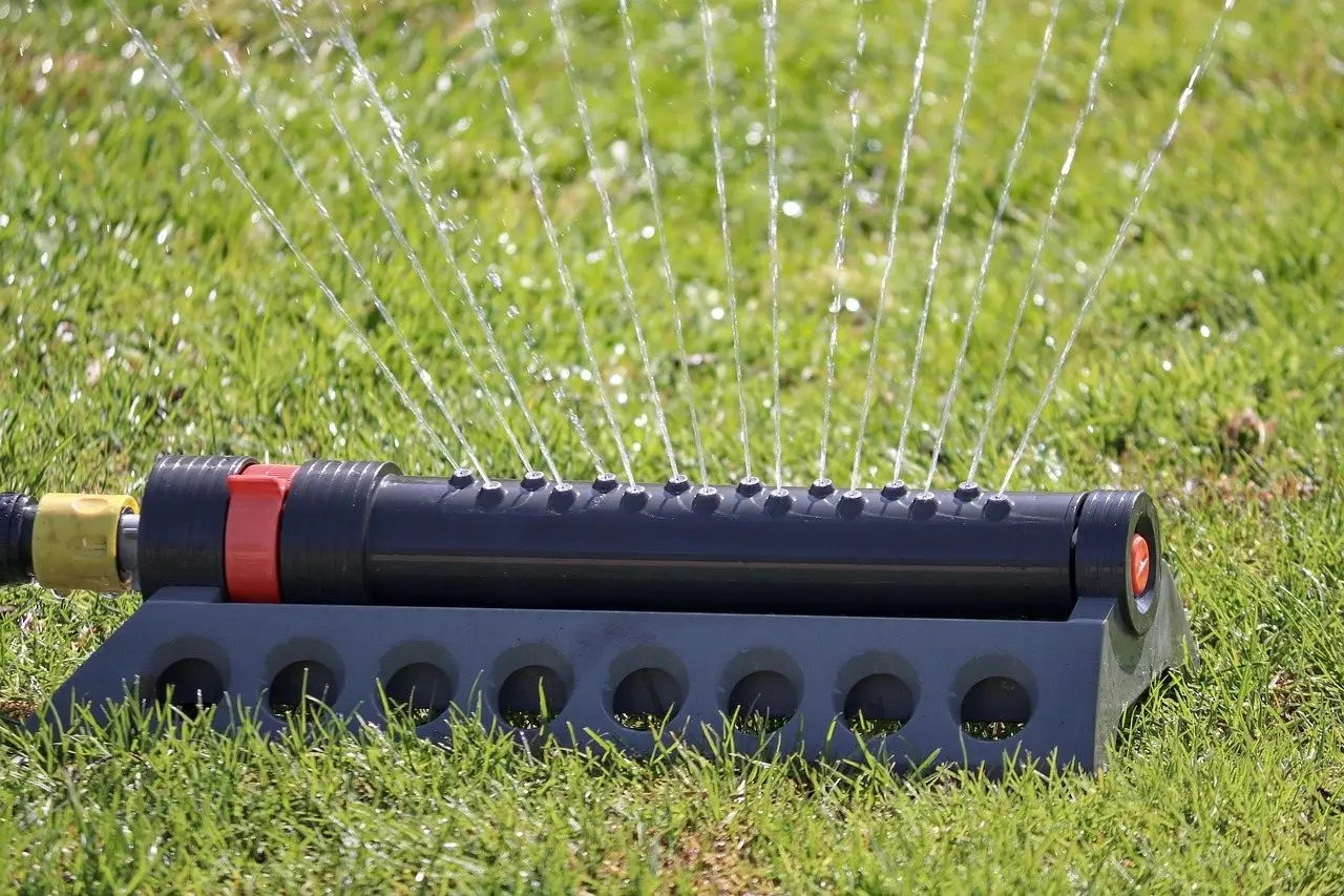 An oscillating sprinkler throwing fine jets of water across a green lawn