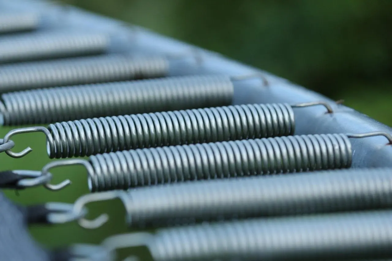 A close view along a row of galvanised trampoline springs hooked to the frame