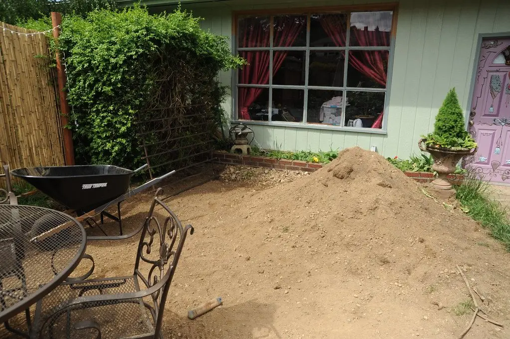 An empty wheelbarrow beside a large mound of dug soil waiting to be moved across a back garden