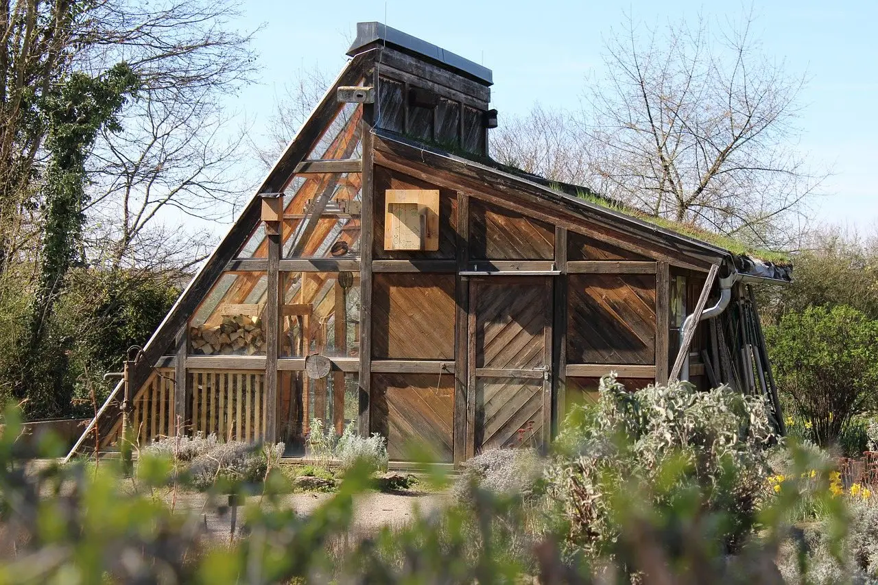 A large timber-framed glasshouse with a steeply pitched roof in a walled garden
