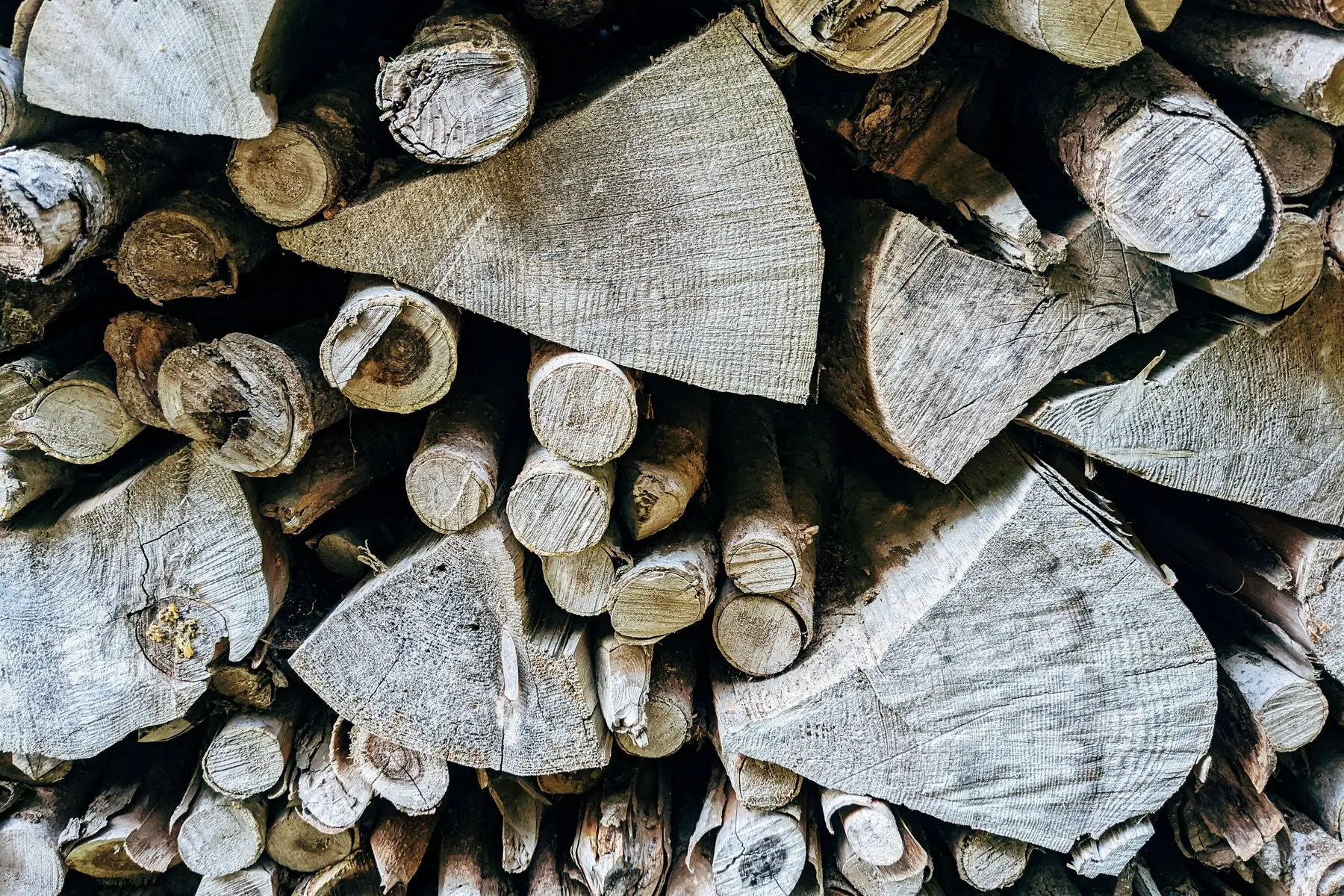 Split firewood stacked end-grain outward, greyed and showing cracks radiating from the centre of each cut face