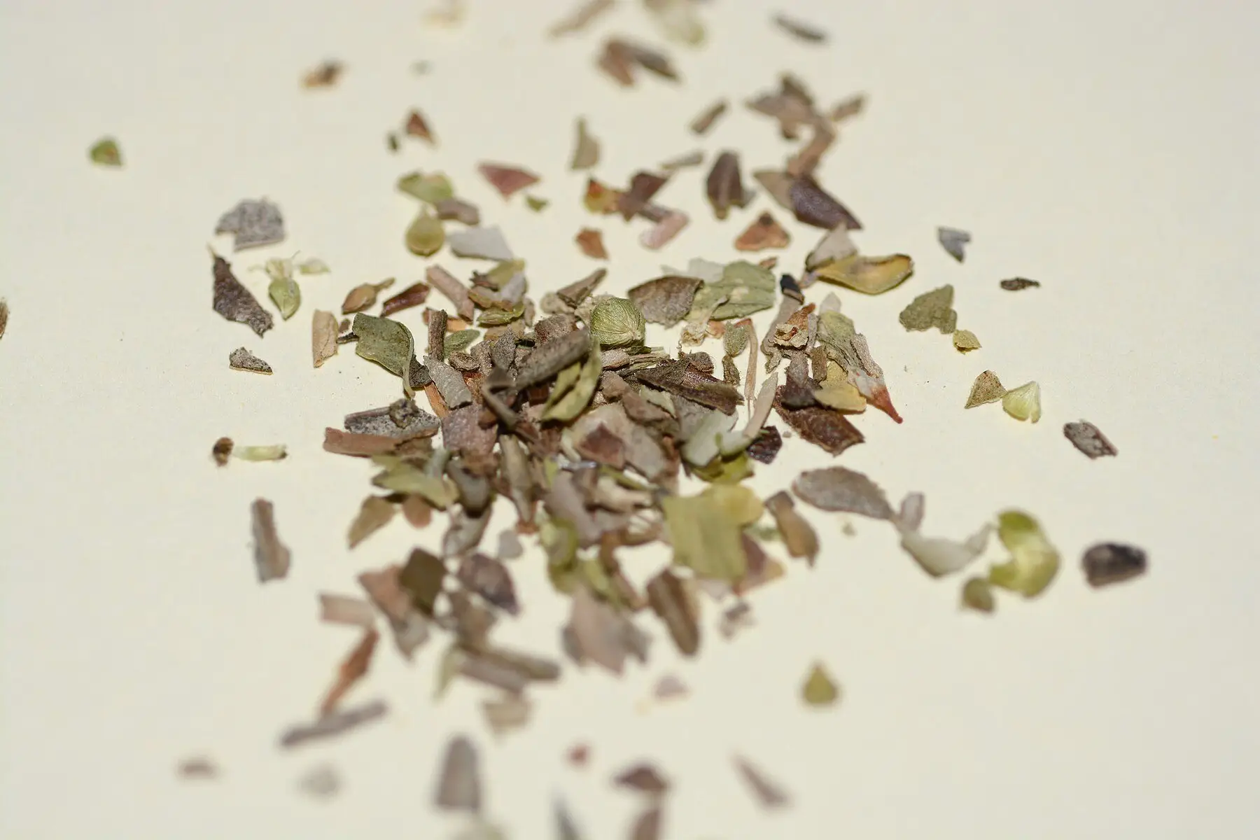 Crumbled dried oregano leaves scattered on a pale surface