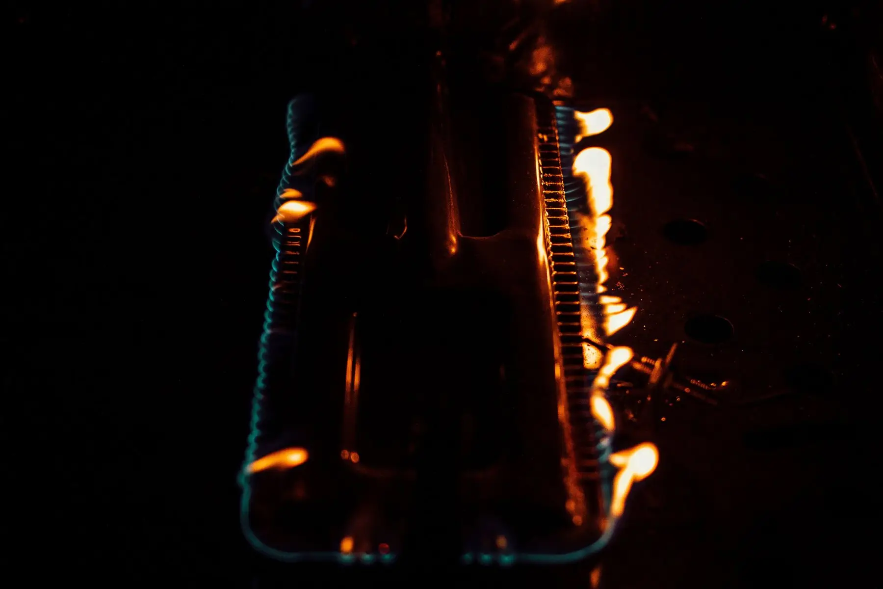 Gas grill burner tubes alight in a dark firebox, the flames running yellow-orange rather than blue