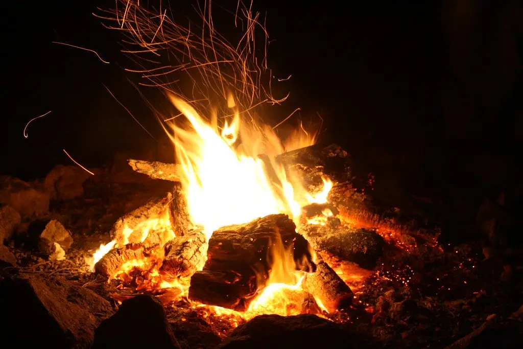 Split logs burning strongly in a fire pit at night, sparks rising from the flames