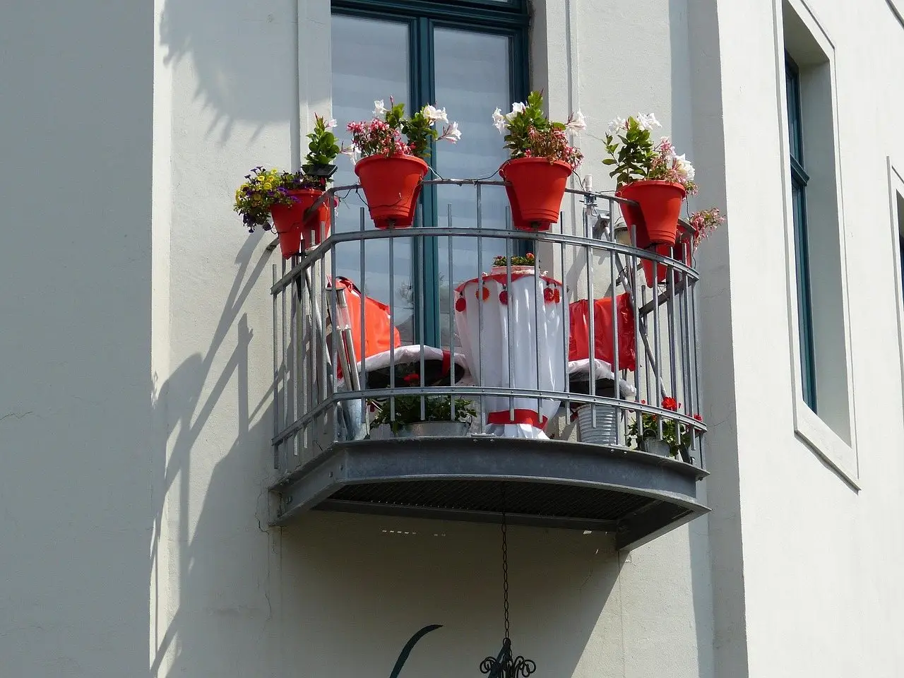 A small balcony with potted plants along the railing and a chair and table