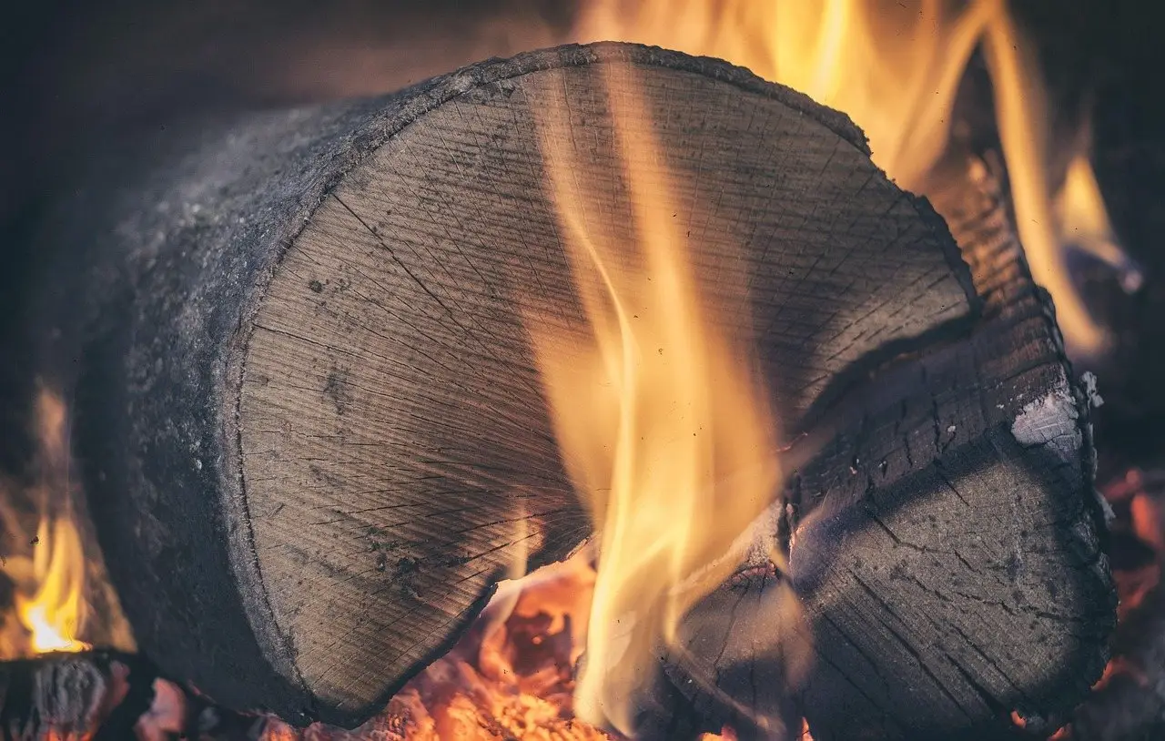 A thick log burning with flames over a bed of red embers