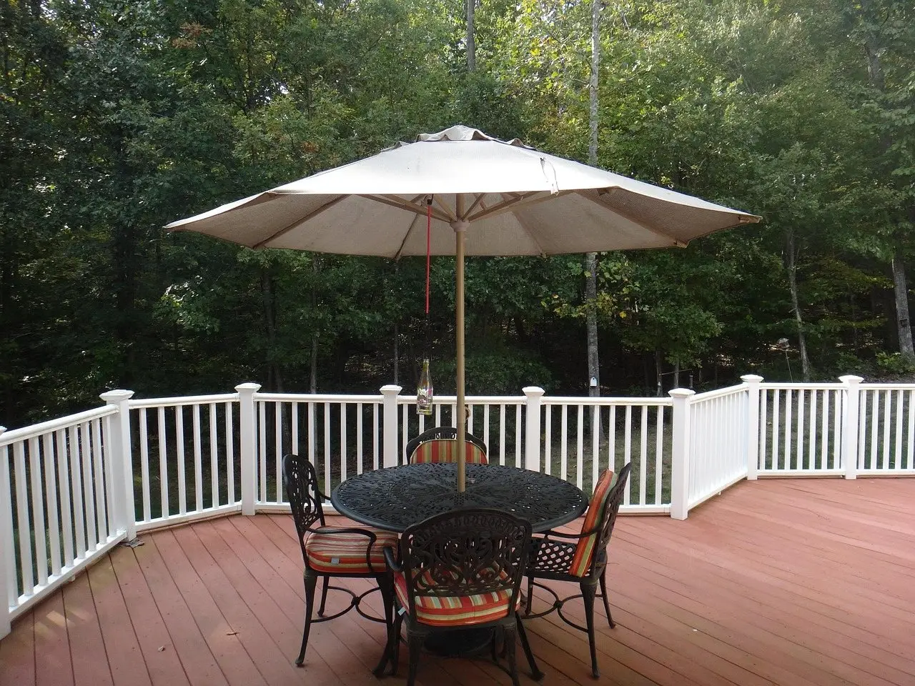 A timber deck with a white railing, a round table, chairs and a parasol