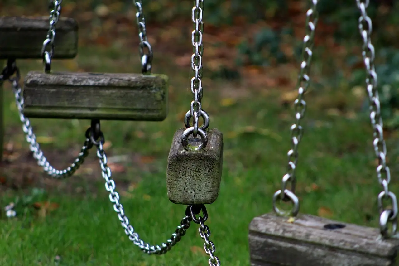 Two wooden swing seats hanging on galvanised chains from a climbing frame