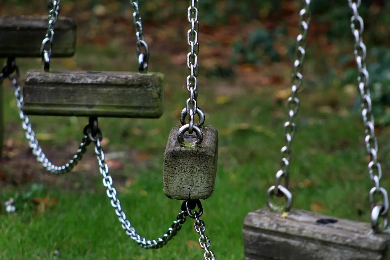 Two wooden swing seats hanging on galvanised chains from a climbing frame