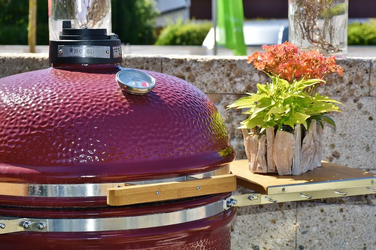 A deep red ceramic kamado cooker with a domed lid, lid thermometer and side shelf