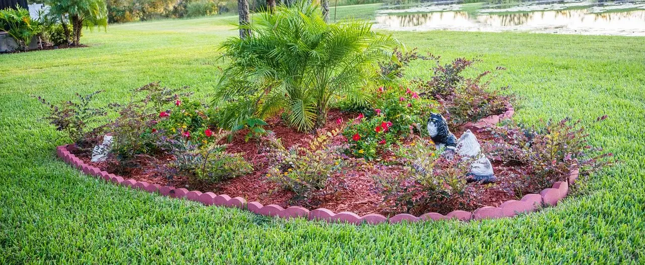 A mulched island bed edged with brick in a lawn, planted with shrubs around a central palm