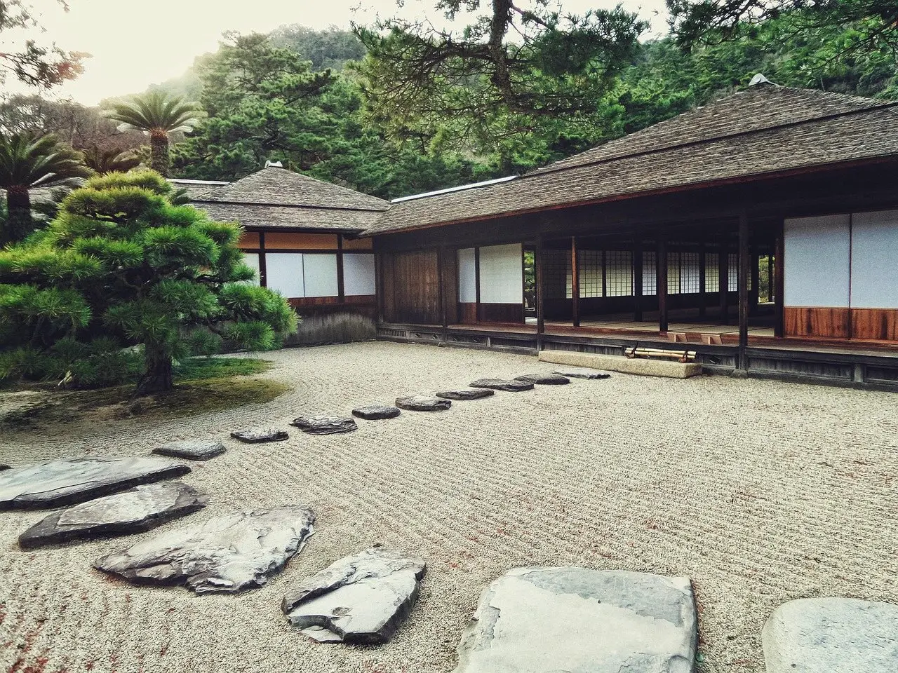 A raked gravel courtyard with flat stepping stones set through it, leading to a timber building