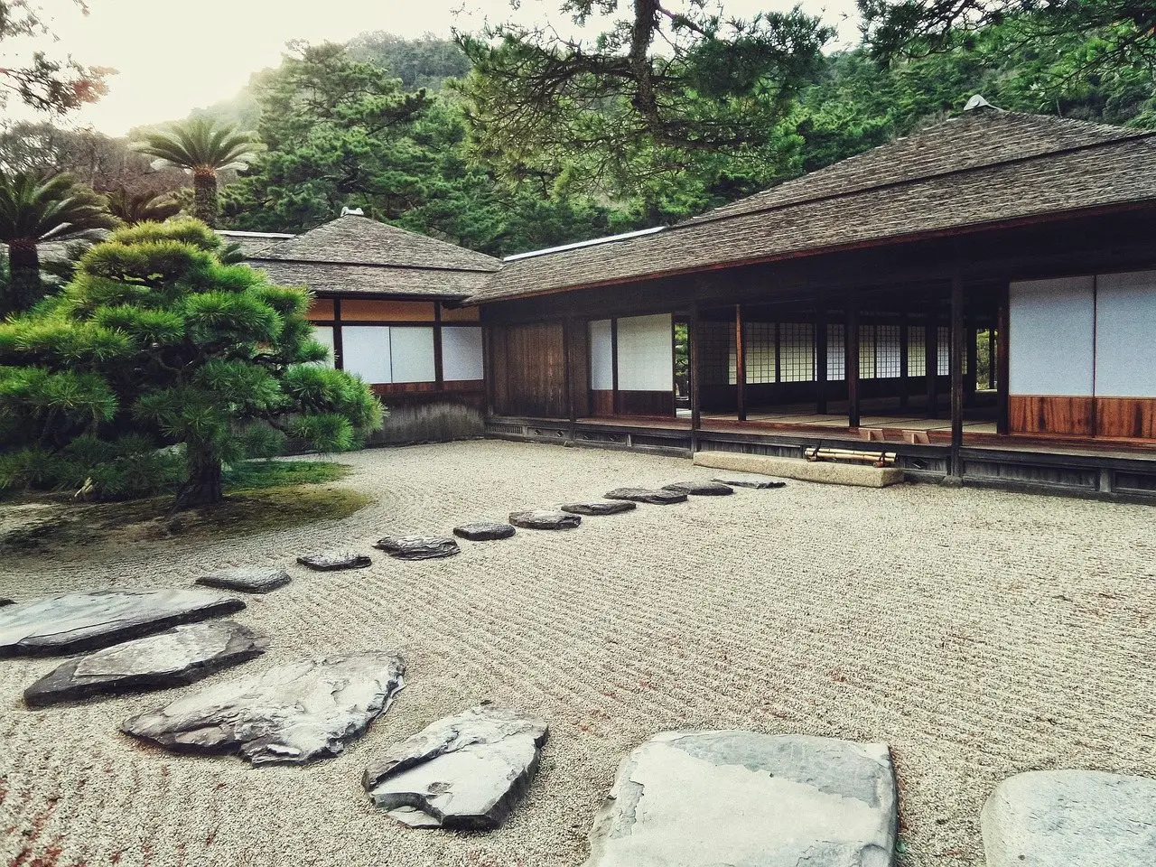A raked gravel courtyard with flat stepping stones set through it, leading to a timber building