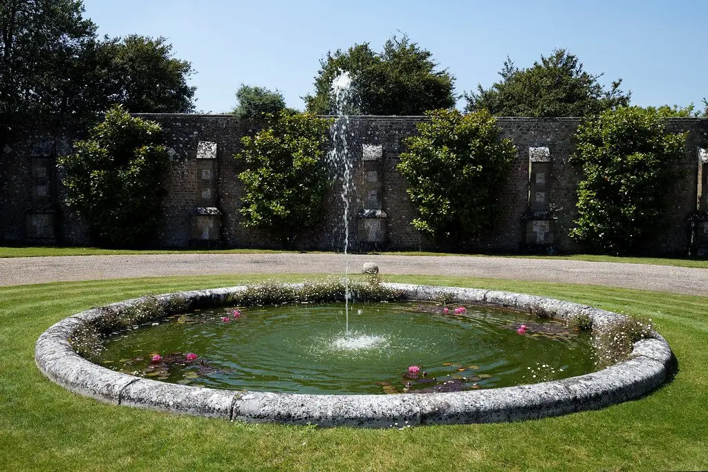 A circular walled garden pond with a fountain jet playing at its centre