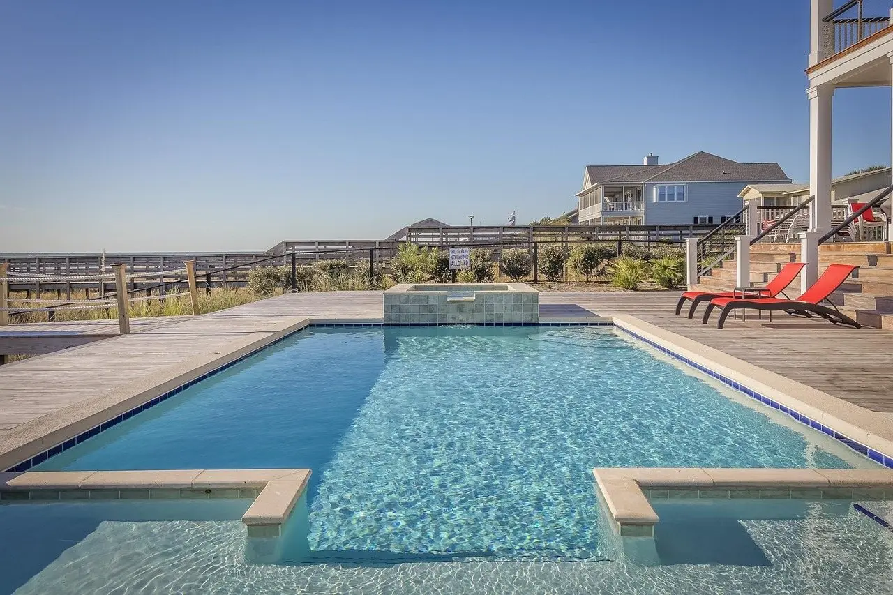 A rectangular pool with a raised spa at one end, timber decking on two sides and loungers beyond