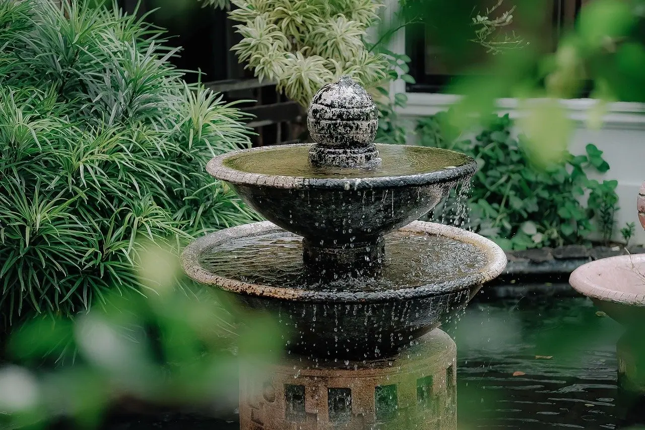 A tiered stone garden fountain running, surrounded by dense green planting