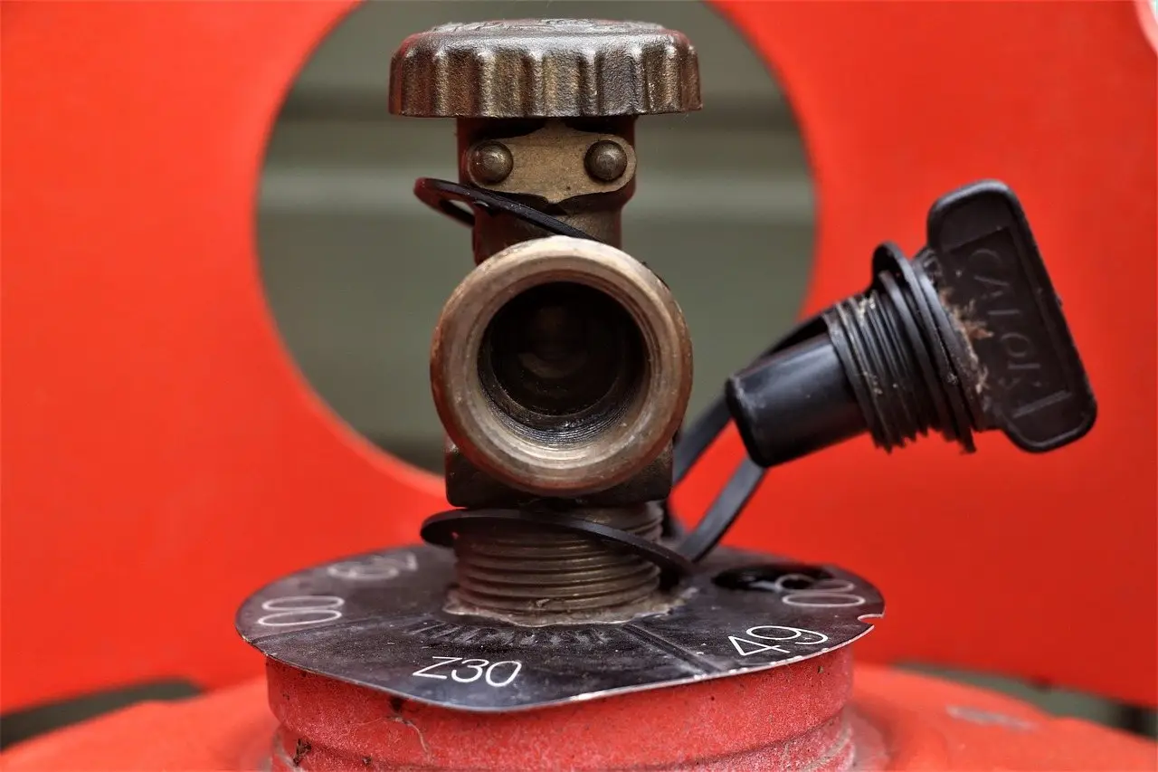 The brass valve and cap on top of a red propane cylinder, seen close up