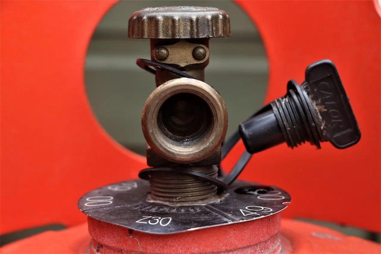 The brass valve and cap on top of a red propane cylinder, seen close up