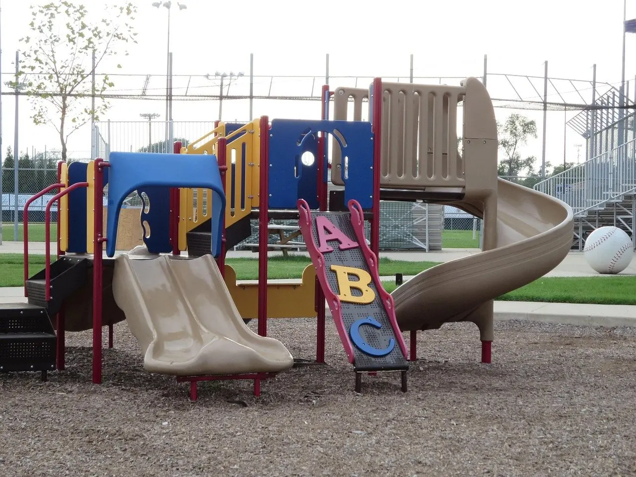 A play structure with slides standing on a loose surfacing material spread across the play area