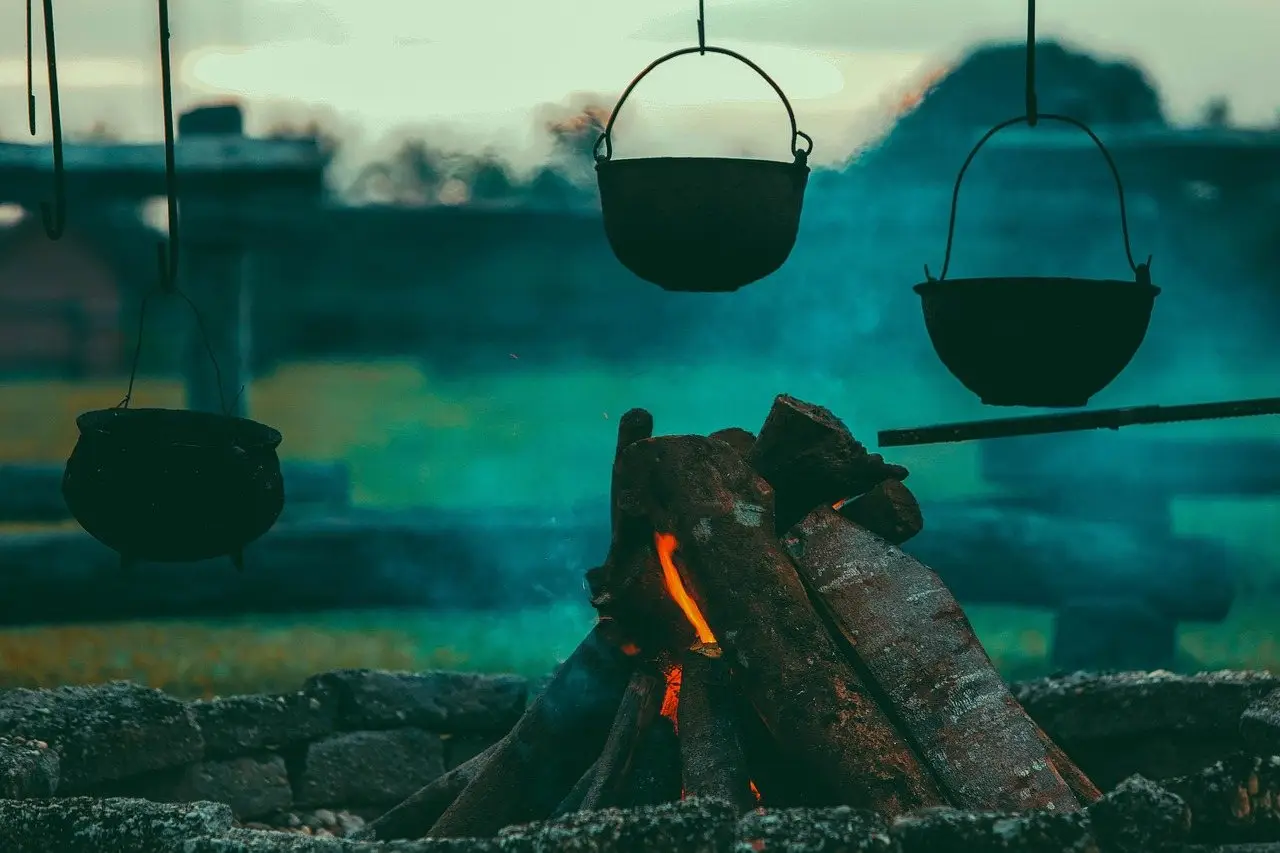 Cast iron pots hanging over an open wood fire burning down to embers
